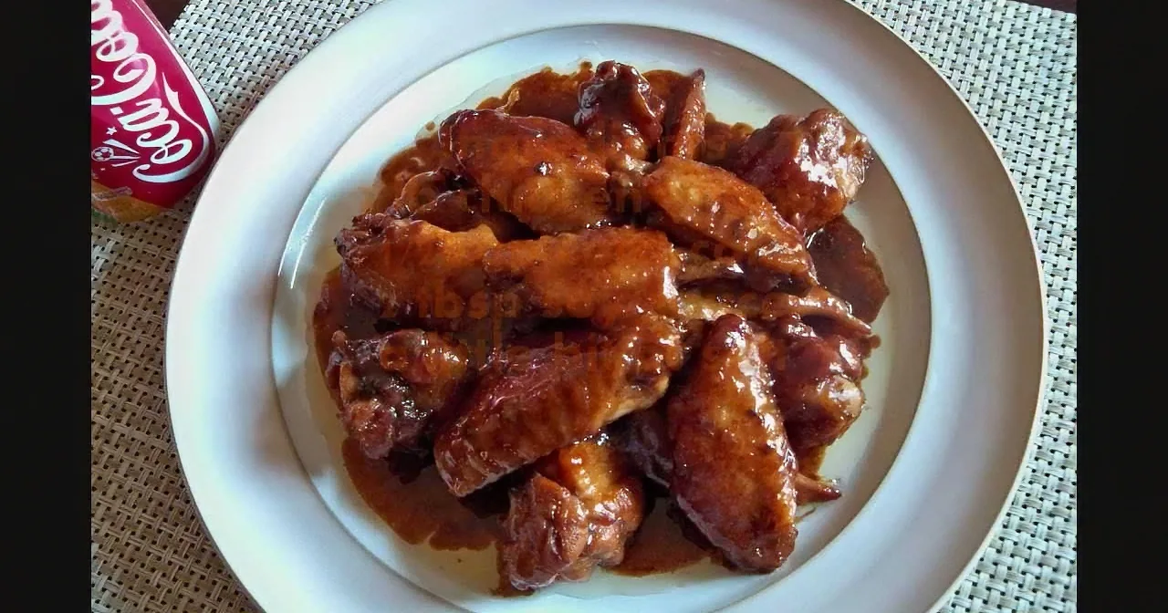A plate of glossy, caramelized chicken wings sits on a woven placemat, accompanied by a Coca-Cola can.