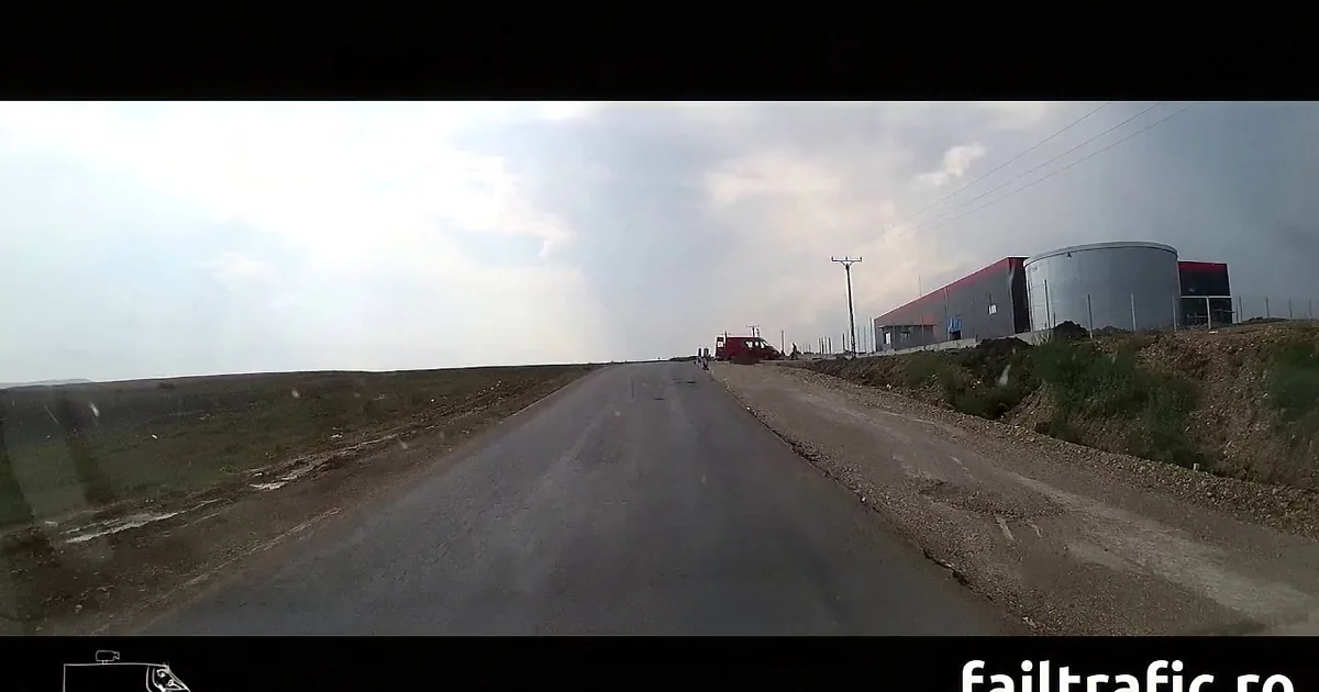 A road stretches into the distance under a cloudy sky, with a red truck and a building on the right.