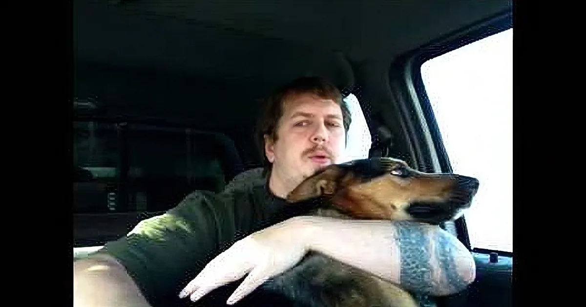 A man in a car with a dog resting its head on his shoulder, both looking out the window.