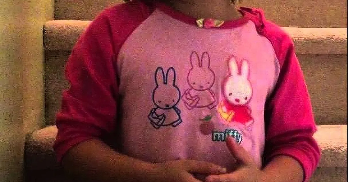 A child wearing a pink and red shirt with cartoon bunnies and the word "miffy" on it.