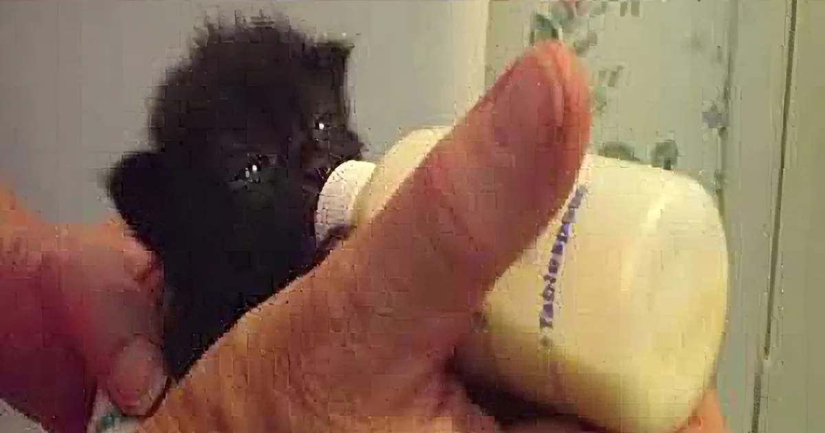 A tiny black kitten is being bottle-fed by a person's hand.