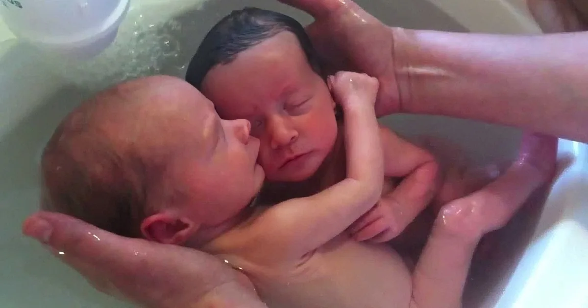 A newborn baby is being bathed by a person holding the baby in a tub.