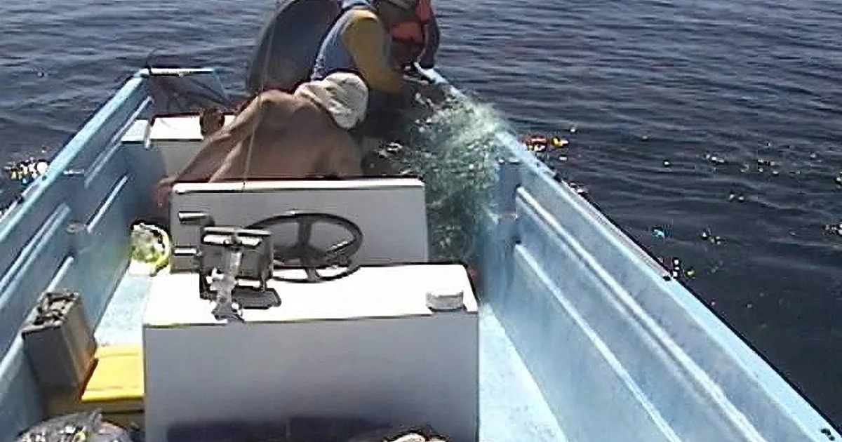 A person in a small boat, wearing a life jacket, is fishing in the ocean.