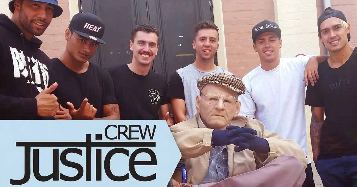 An elderly man in a beige jacket and cap is surrounded by six young men in casual attire, smiling and posing together.