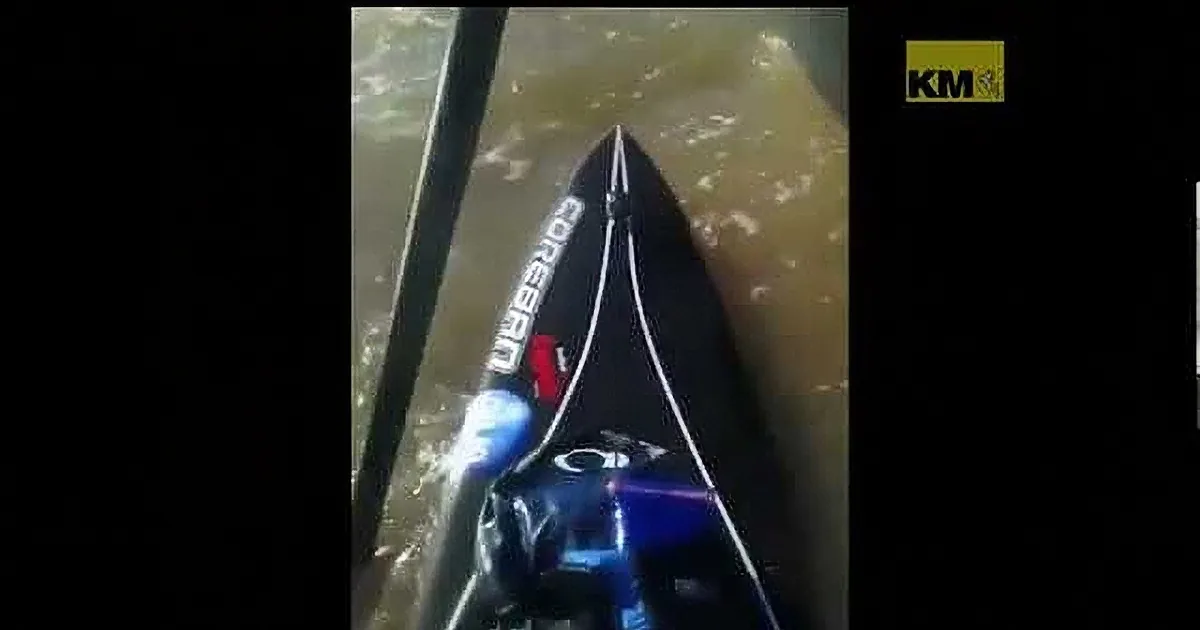 A kayak with "Cobra" text on its nose is partially submerged in murky water, with a person's legs visible inside.
