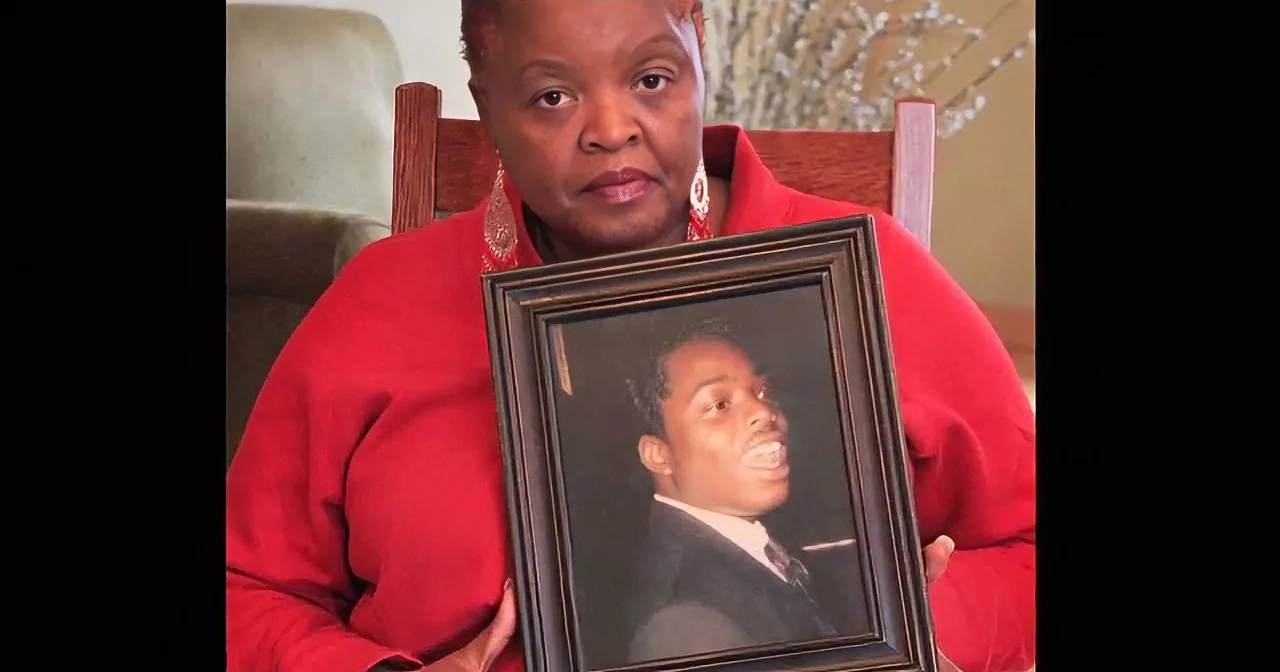 A woman in red holds a framed portrait, sitting in a chair with a decorative background.
