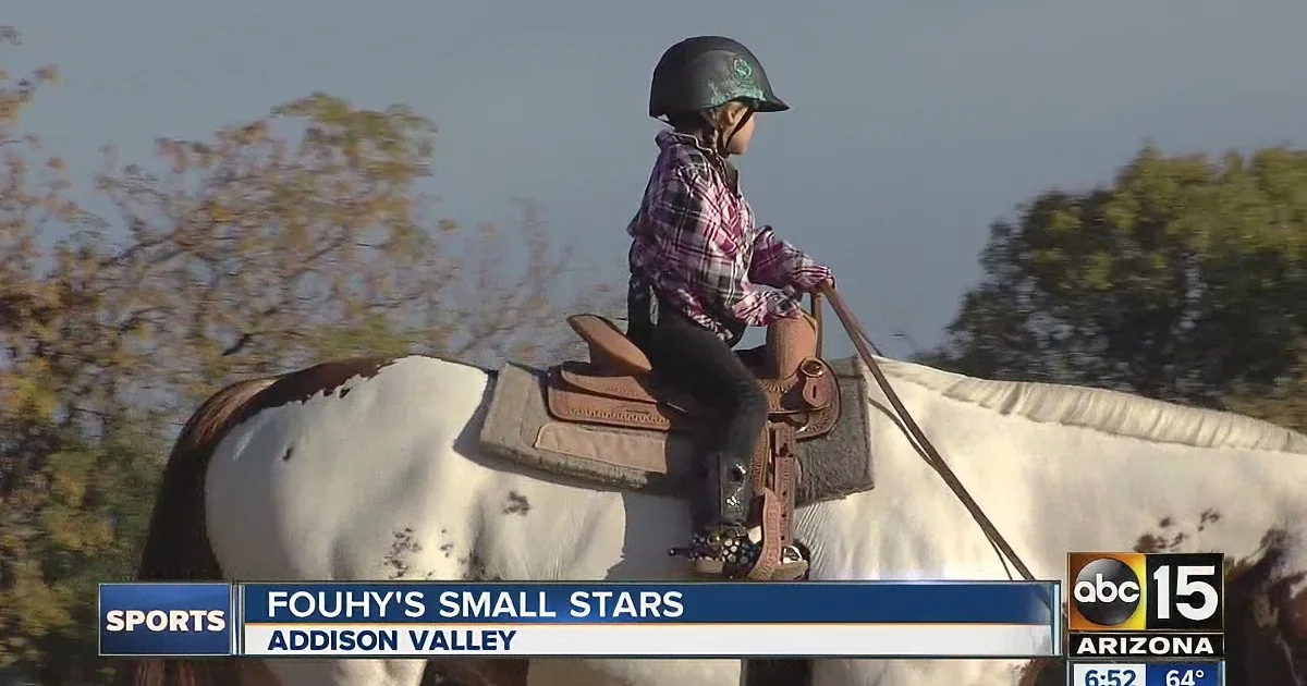 A young girl in a plaid shirt rides a white horse, wearing a helmet, in an outdoor setting.
