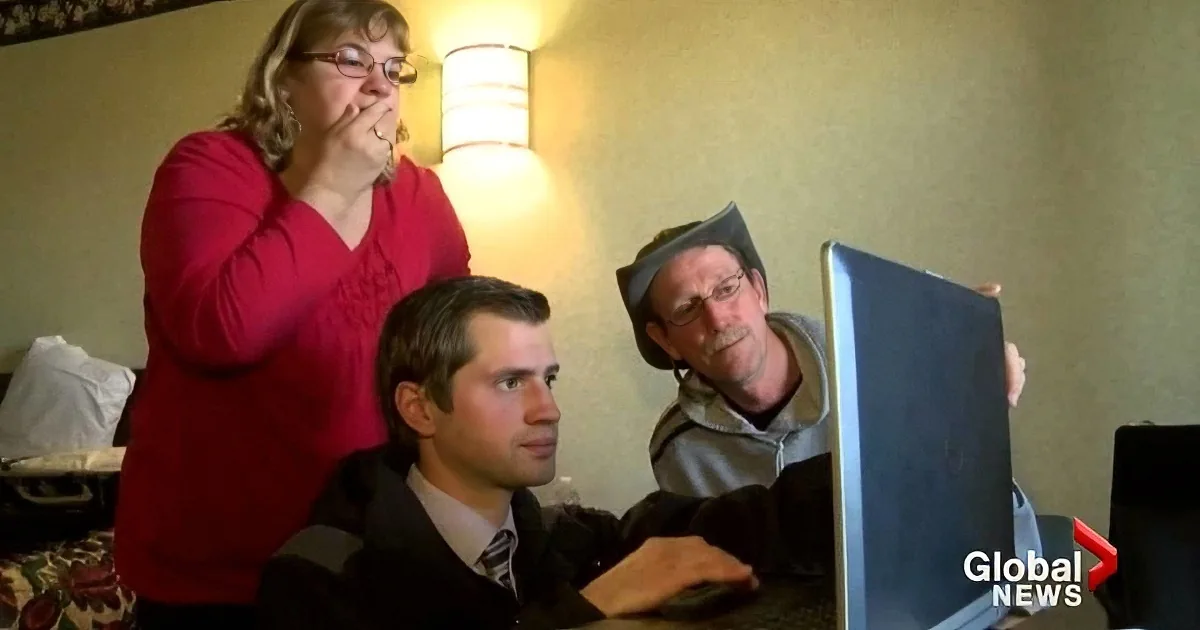 A woman in a red sweater stands behind a man in a suit, both looking at a laptop screen.
