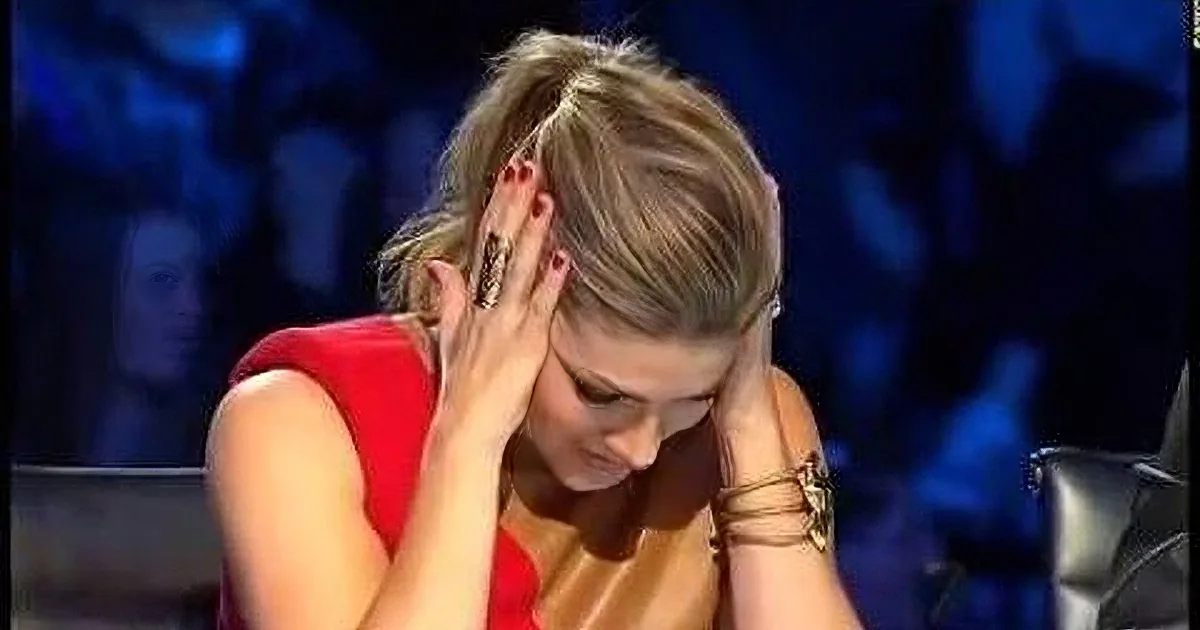 A woman in a red dress covers her face with her hands, appearing distressed, against a dark, blurred background.