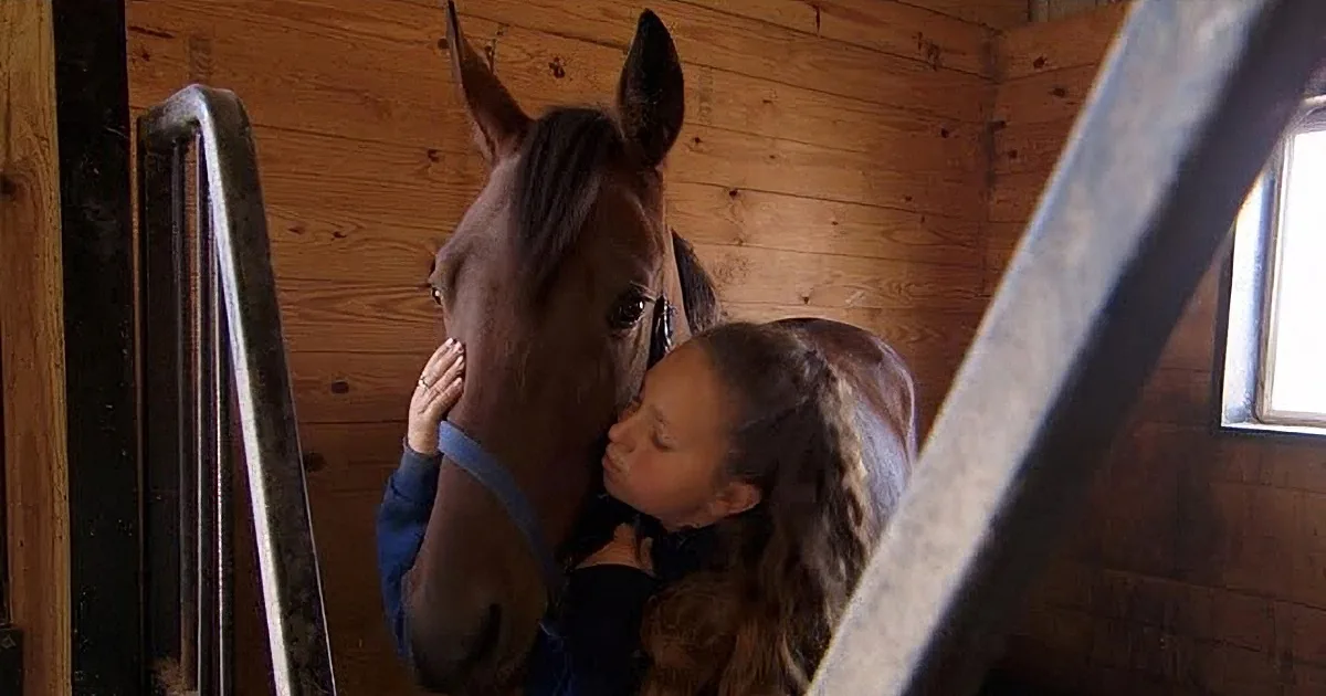 A young girl is gently petting a horse in a wooden stable.