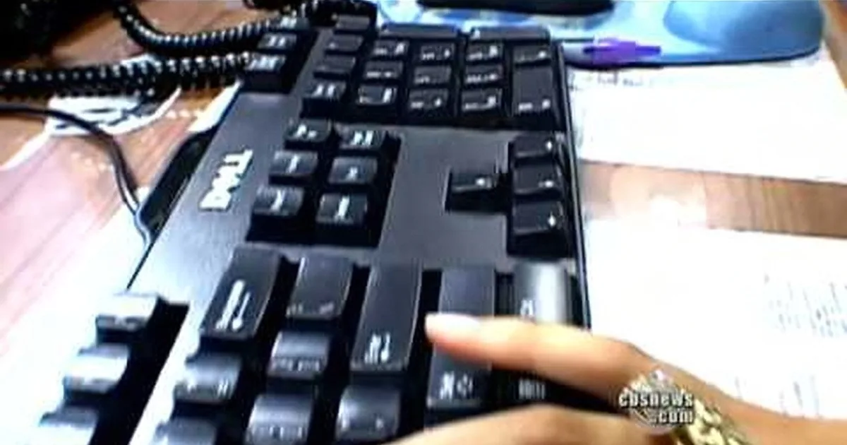 A Dell keyboard is shown with a finger pressing a key, surrounded by office items like a phone and papers.