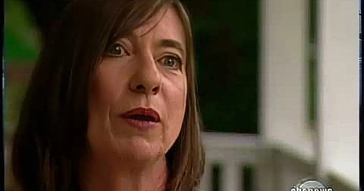 A woman with long brown hair is speaking, wearing a dark top, and appears to be in a professional setting.