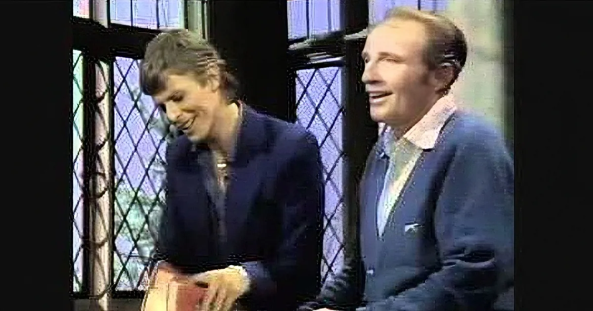 Two individuals, one in a dark suit, are seated and smiling, with a window in the background.