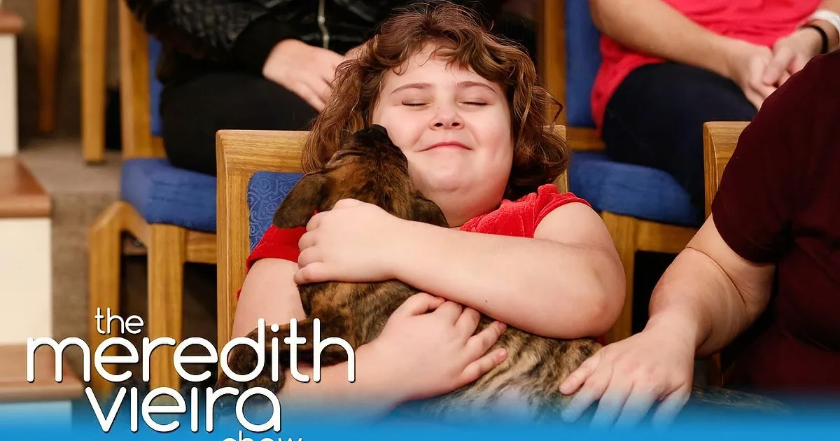 A child in red hugs a cat, surrounded by people in chairs, with "The Meredith Vieira Show" logo.