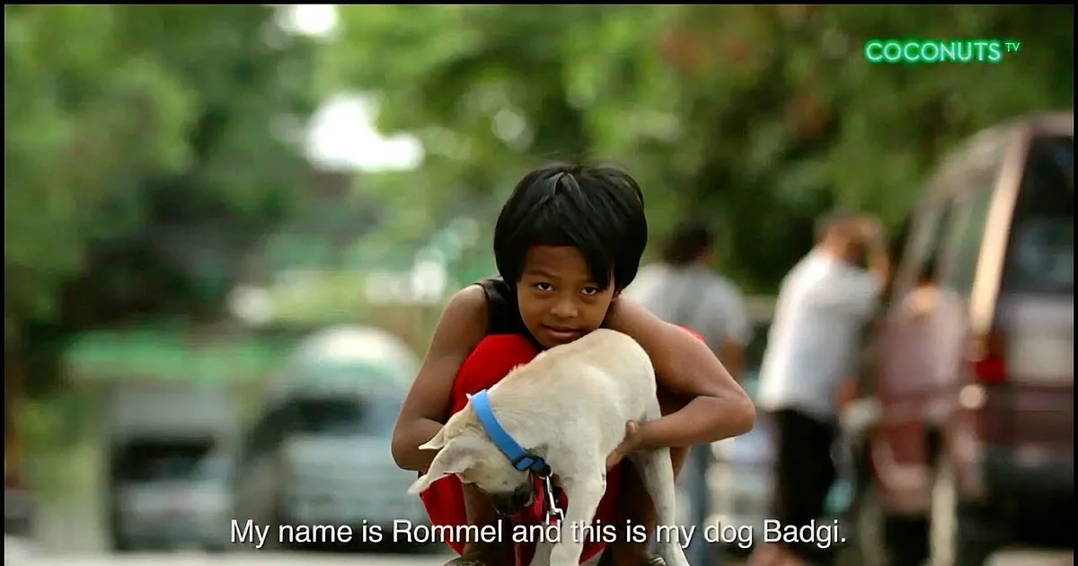 A child named Rommel rides a motorcycle with his dog Badgi, both wearing harnesses.