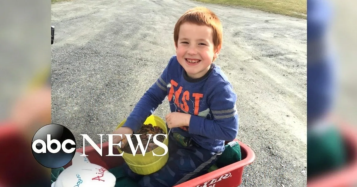 A young boy smiles brightly while sitting in a red wagon filled with toys and pinecones.