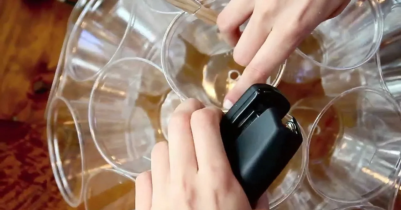 A person uses a black tool to manipulate a clear, multi-cup object on a wooden surface.