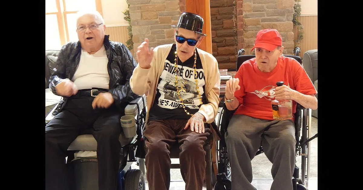 Three elderly men in wheelchairs, one in a black jacket, another in a "Beware of Dog" shirt, and the third in a red cap...