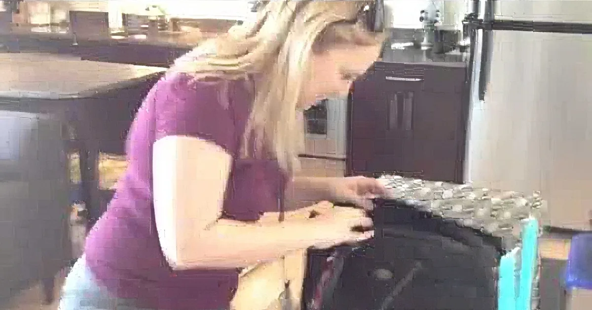 A woman in a purple shirt is bending over, holding a piece of foil, in a kitchen setting.