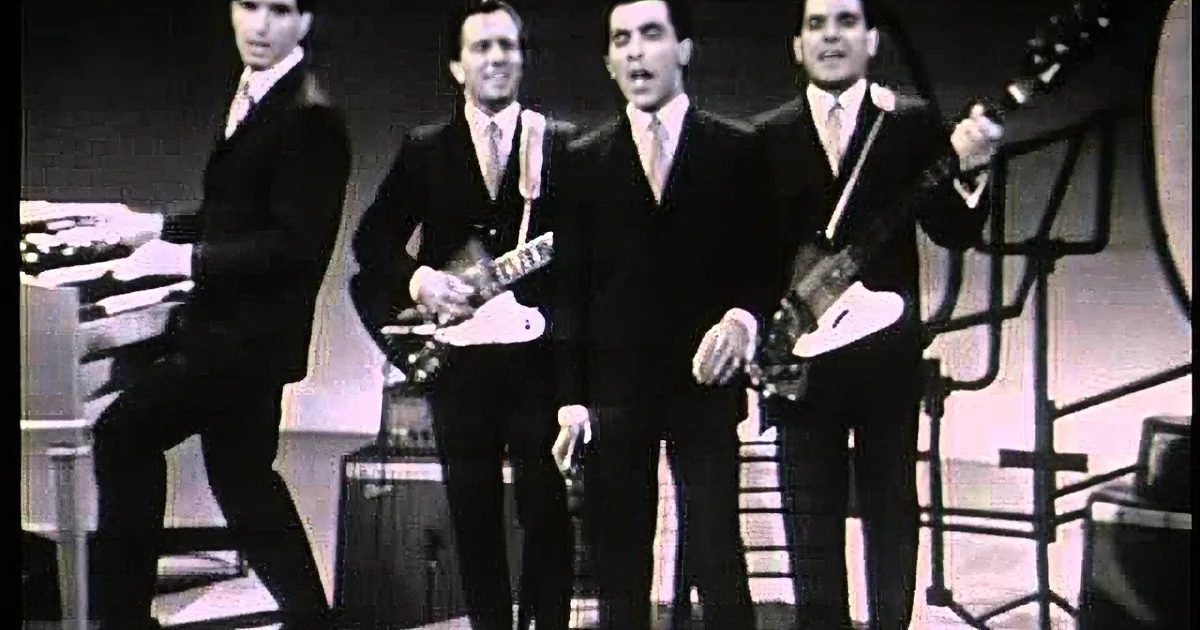 Four men in suits play guitars and sing on stage, black and white.