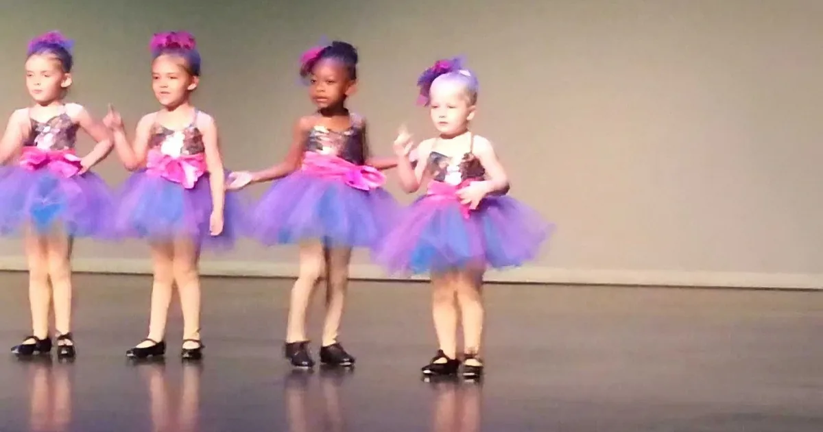 Four young girls in colorful tutus and tap shoes perform a dance routine on stage.