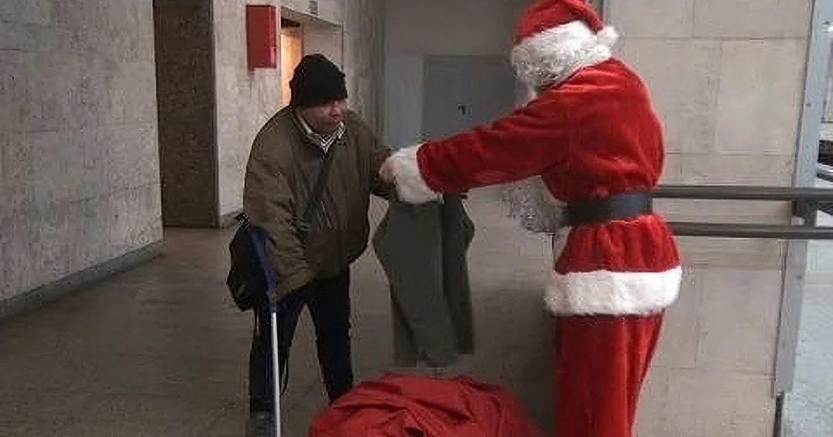 A person dressed as Santa Claus hands a bag to a man with a cane in a hallway.