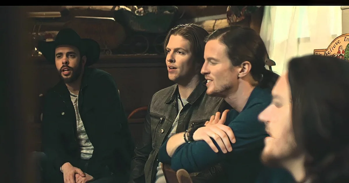 Three men in a dimly lit room, one wearing a cowboy hat, appear to be engaged in conversation.