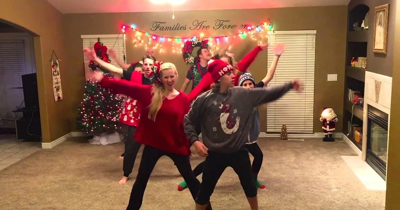 A group of people in festive attire dances joyfully in a Christmas-decorated living room.