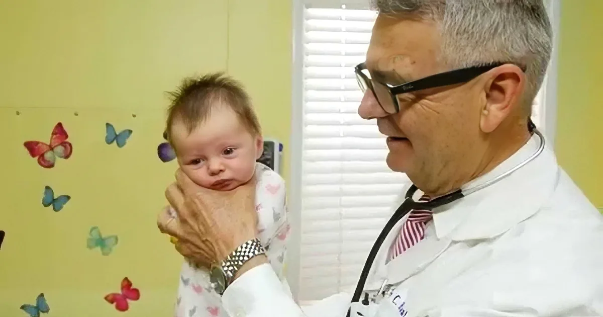 A doctor in a white coat examines a baby while wearing glasses and a stethoscope.