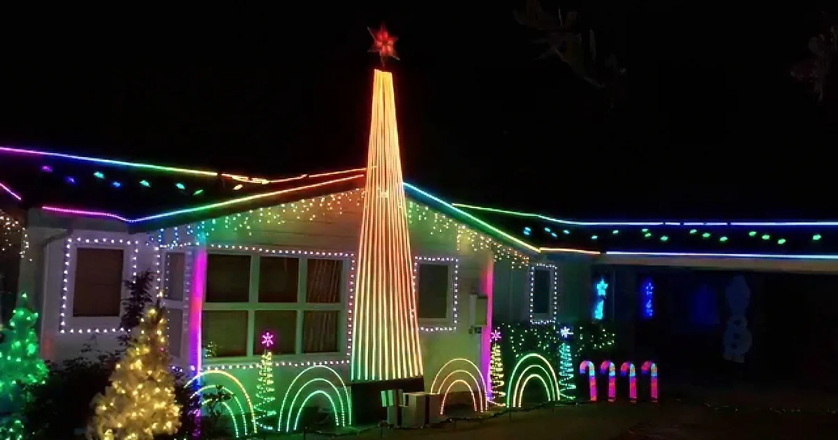A brightly lit house adorned with colorful Christmas lights and decorations, including a tall tree and festive ornaments.