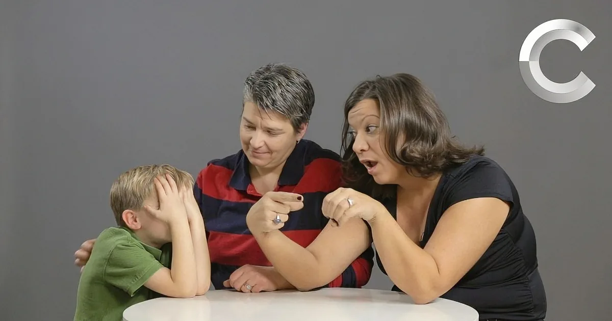 A woman in a black shirt is pointing at another woman, who is leaning over a table with a child in a green shirt.
