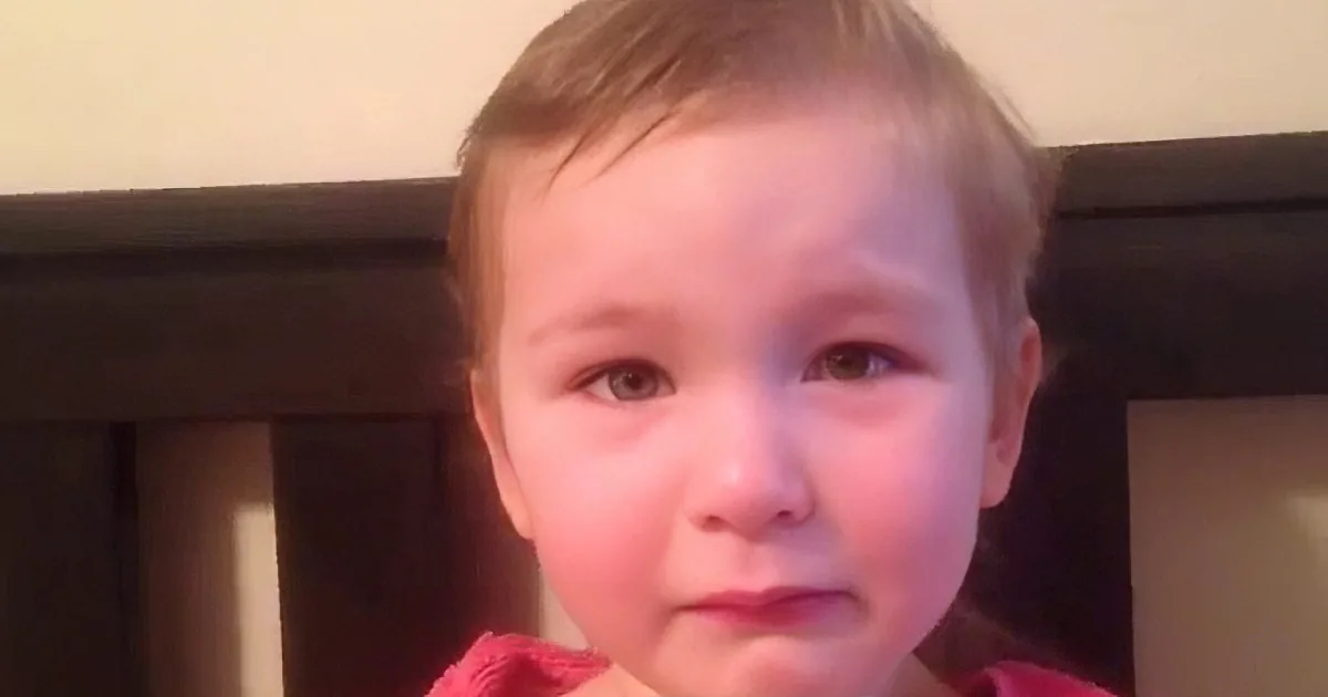 A young child with light hair and a pink garment is looking directly at the camera.