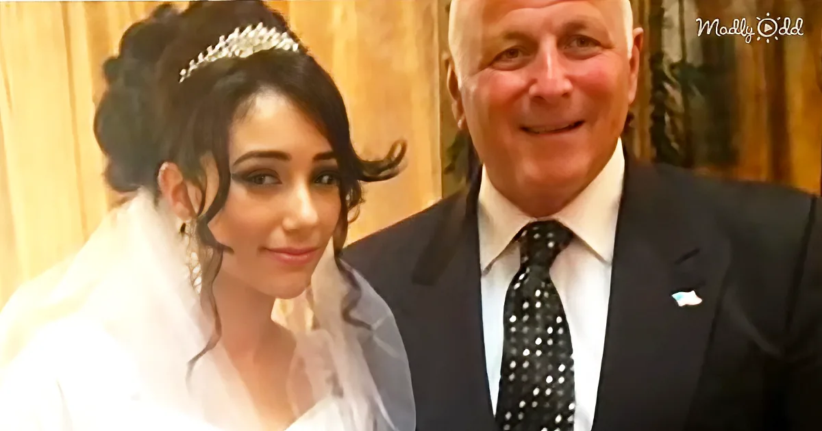 A bride in a white dress and tiara stands next to a man in a black suit and tie, both smiling.