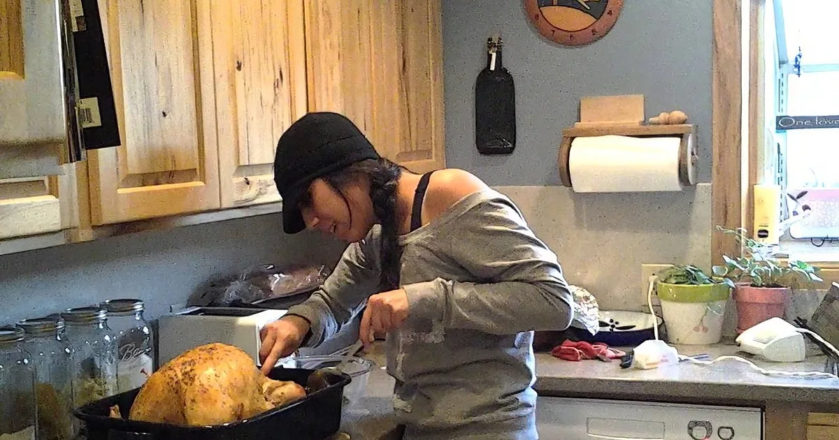 A person in a kitchen prepares a roasted turkey in a black pan on the counter.