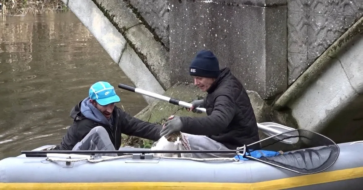 Two people in an inflatable kayak under a bridge, one holding a fishing rod.