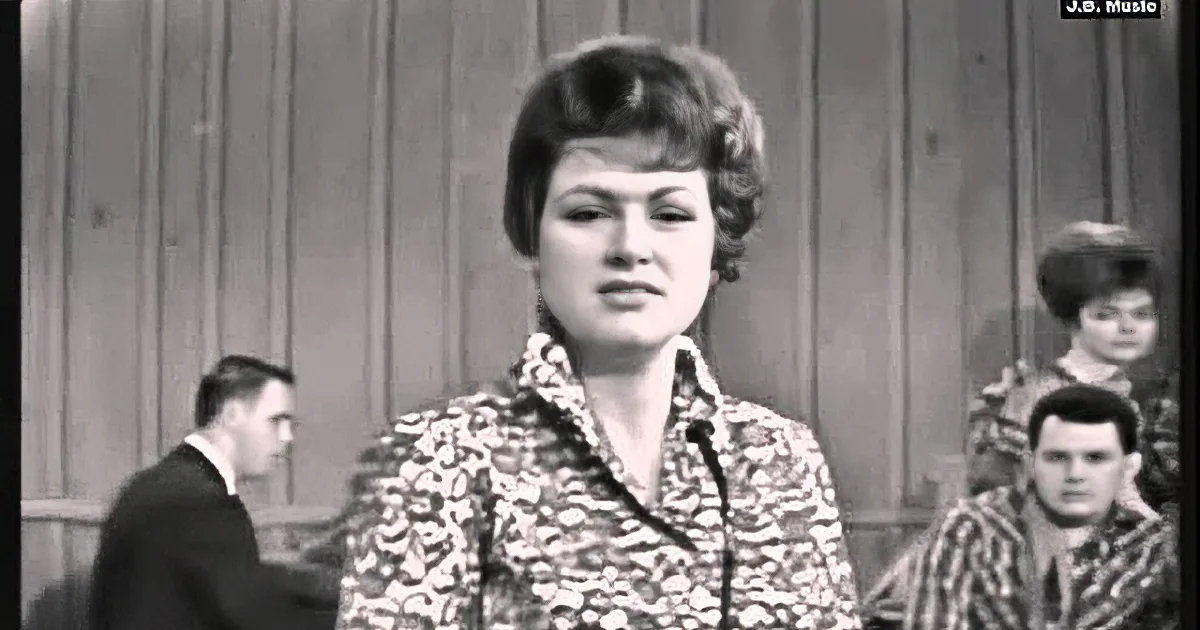 A woman in a patterned blouse stands in the foreground, with blurred figures in the background.