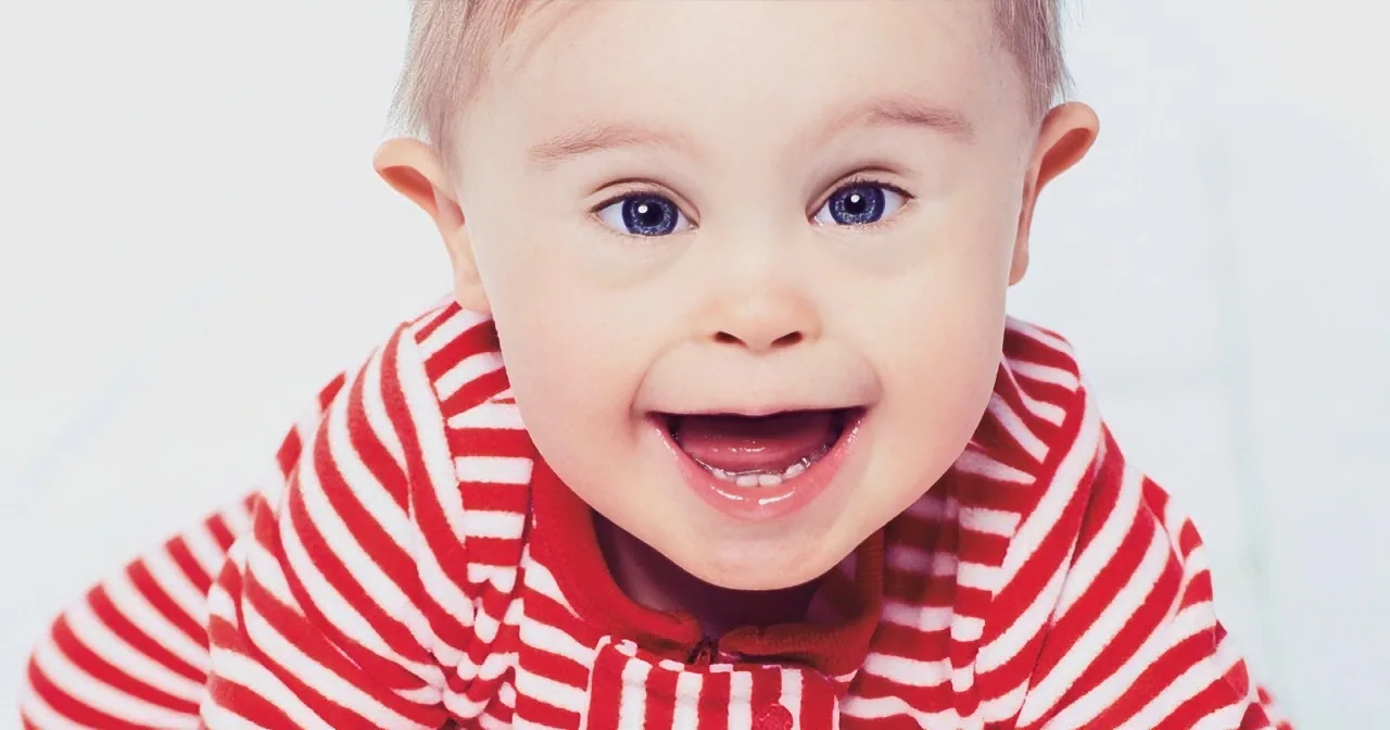 A baby in a red and white striped shirt is smiling widely, showing teeth.
