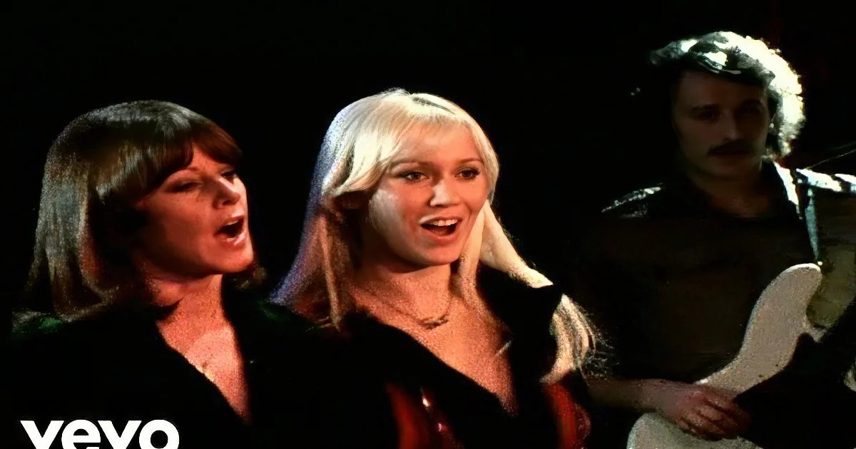 A woman with long blonde hair sings passionately, accompanied by another woman and a man playing guitar.