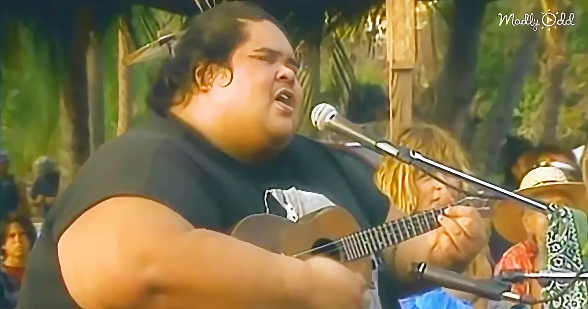 A man in a black shirt sings passionately into a microphone while playing a guitar.