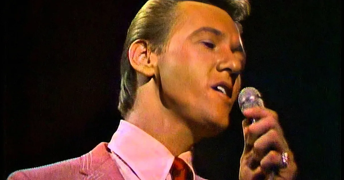 A man in a pink suit sings into a microphone, his expression focused and passionate.