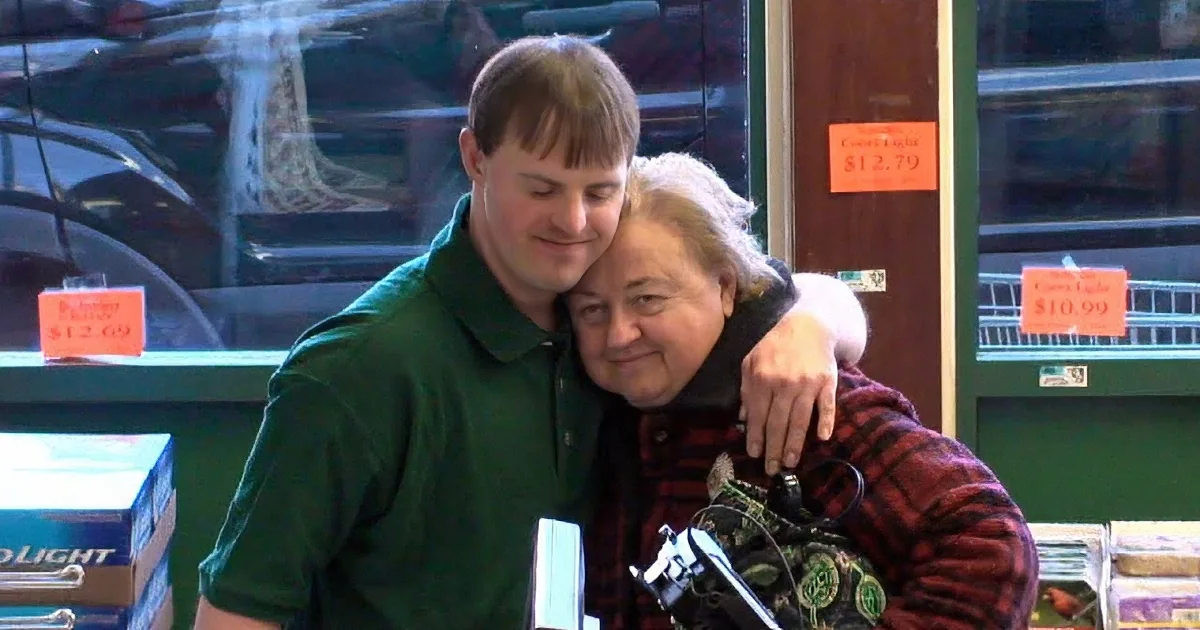 A man in a green shirt hugs an older woman in a plaid jacket at a store checkout.