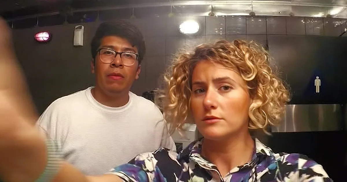 A person with curly hair and a floral top is in the foreground, while another person in a white shirt is in the background.