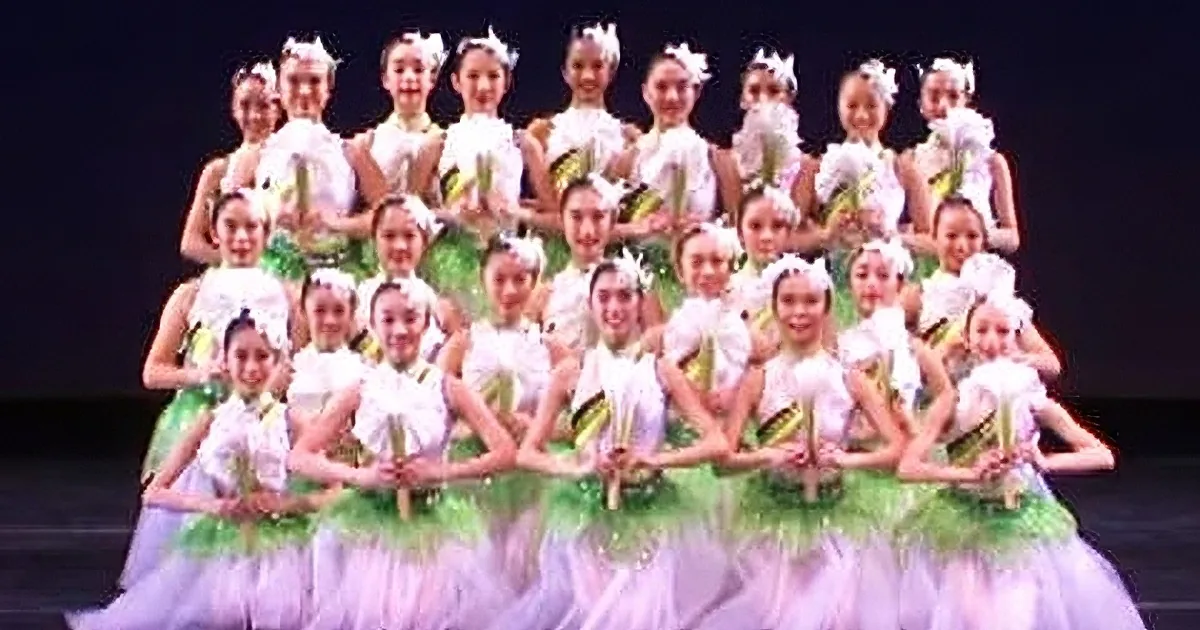 A group of dancers in white and green costumes perform a synchronized dance on stage.