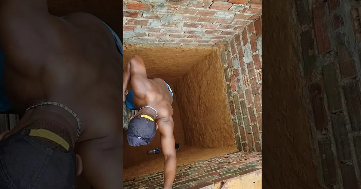 A muscular man in shorts and a cap is climbing up a brick wall.