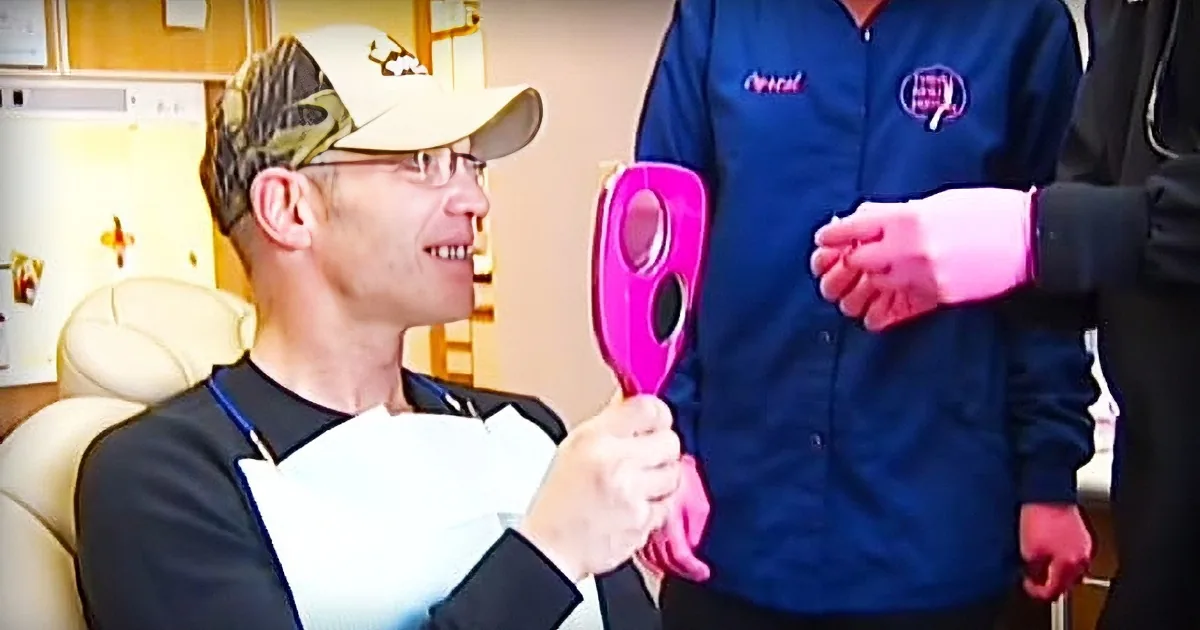 A man in a cap and glasses smiles while holding a pink object, possibly a tool or device, in a clinical setting.