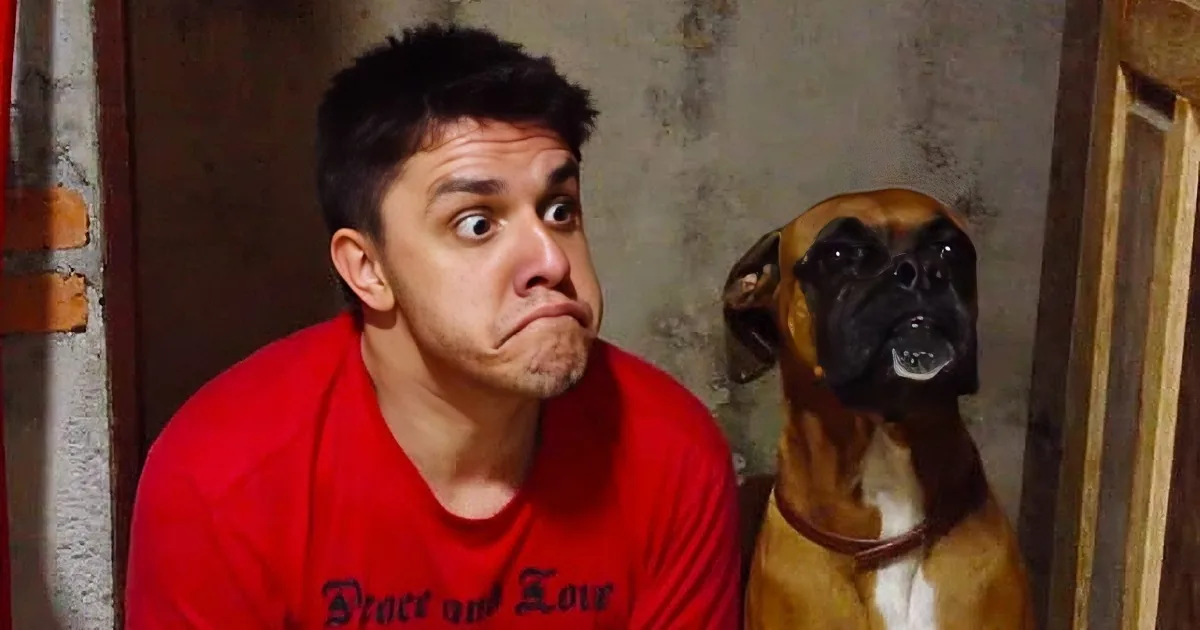 A man in a red shirt makes a funny face next to a dog in a similar pose.