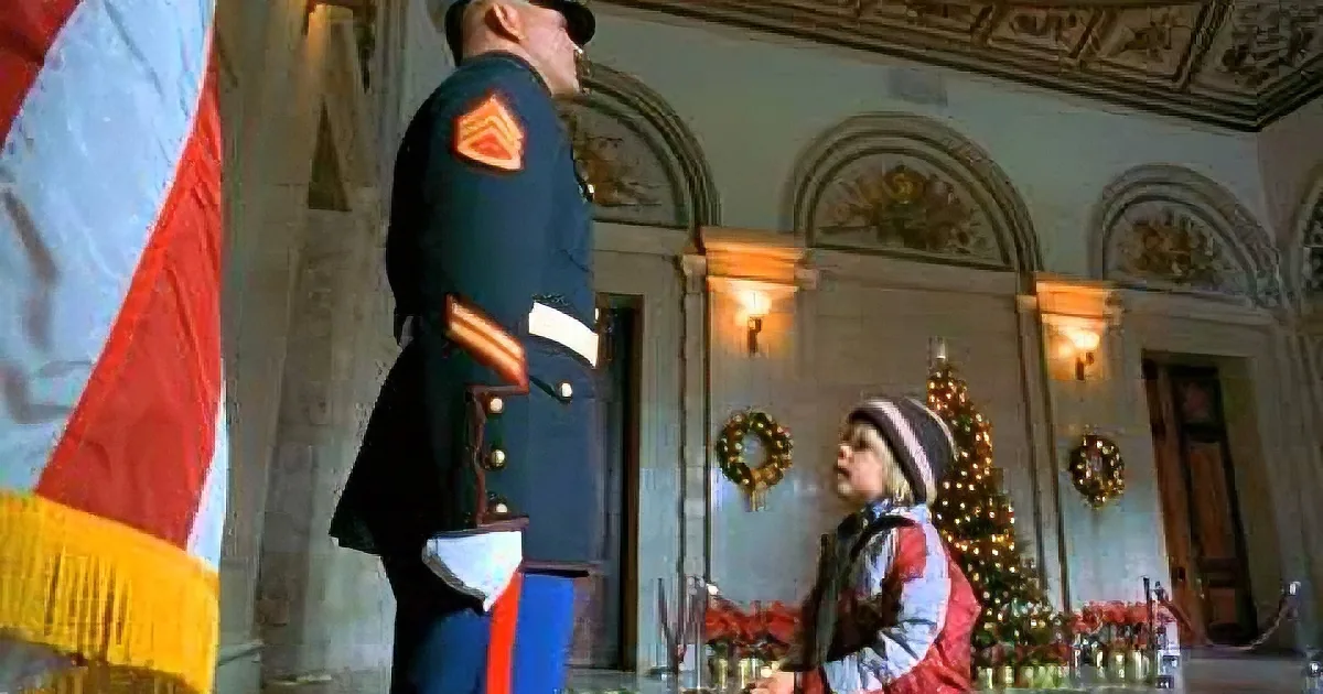 A soldier in uniform stands at attention next to a child in a festive room with a Christmas tree.