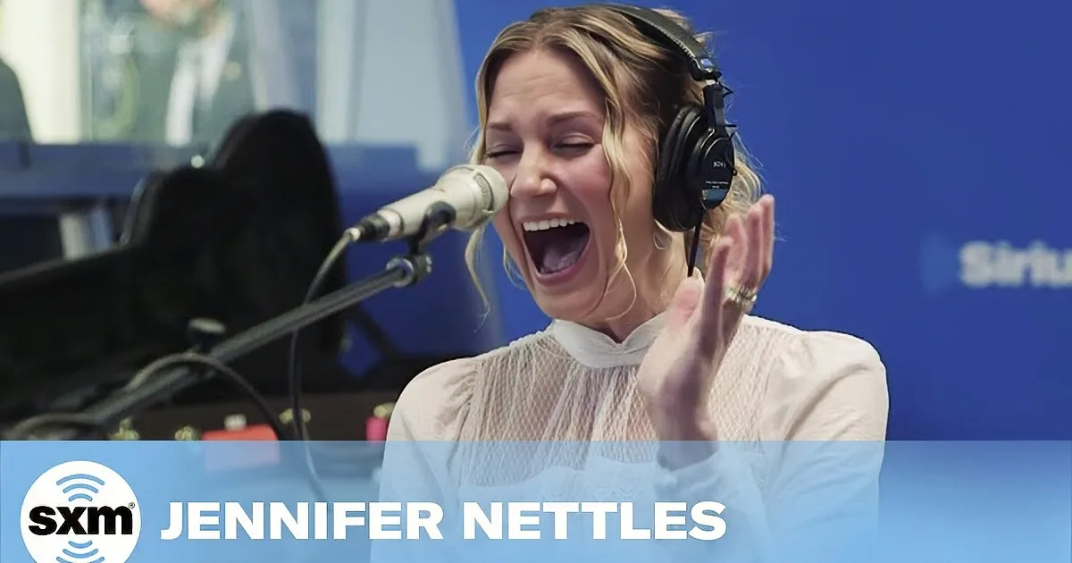 A woman wearing headphones sings into a microphone in a studio setting.