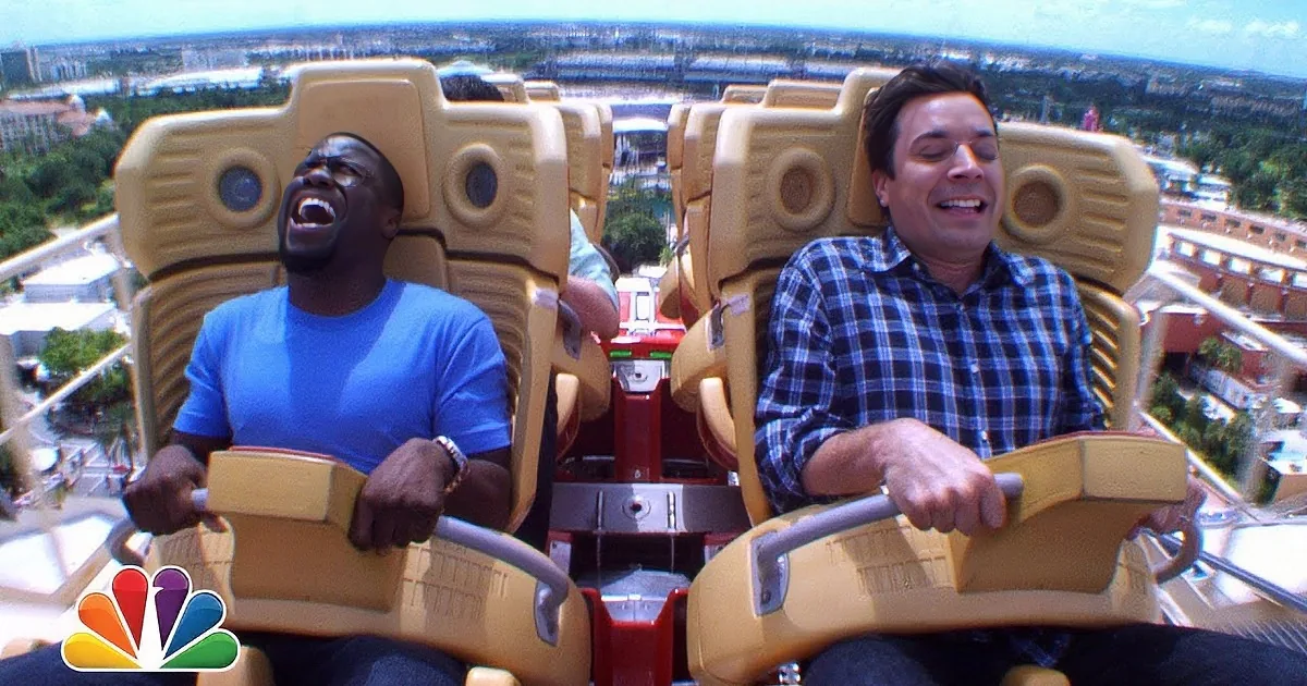 Two men on a roller coaster, one laughing, one with mouth open, enjoying the ride.