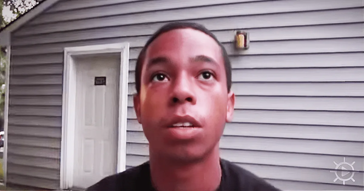 A person is in front of a gray-sided house with a white door and a light fixture above it.